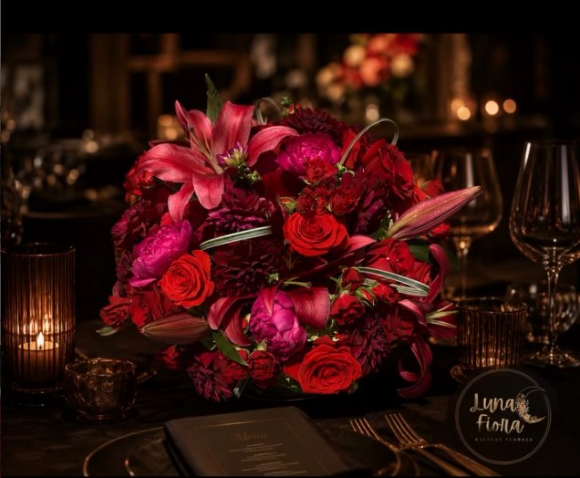 Dramatic crimson and fuchsia centerpiece of lilies, dahlias and roses on a dark evening table setting