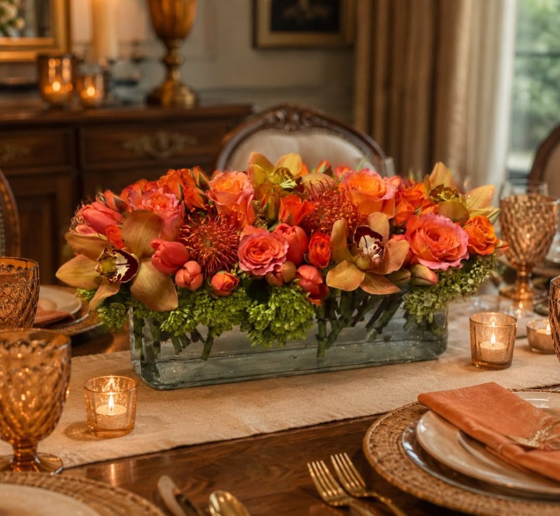 Long low centerpiece of coral roses and orchids on a candlelit dining table